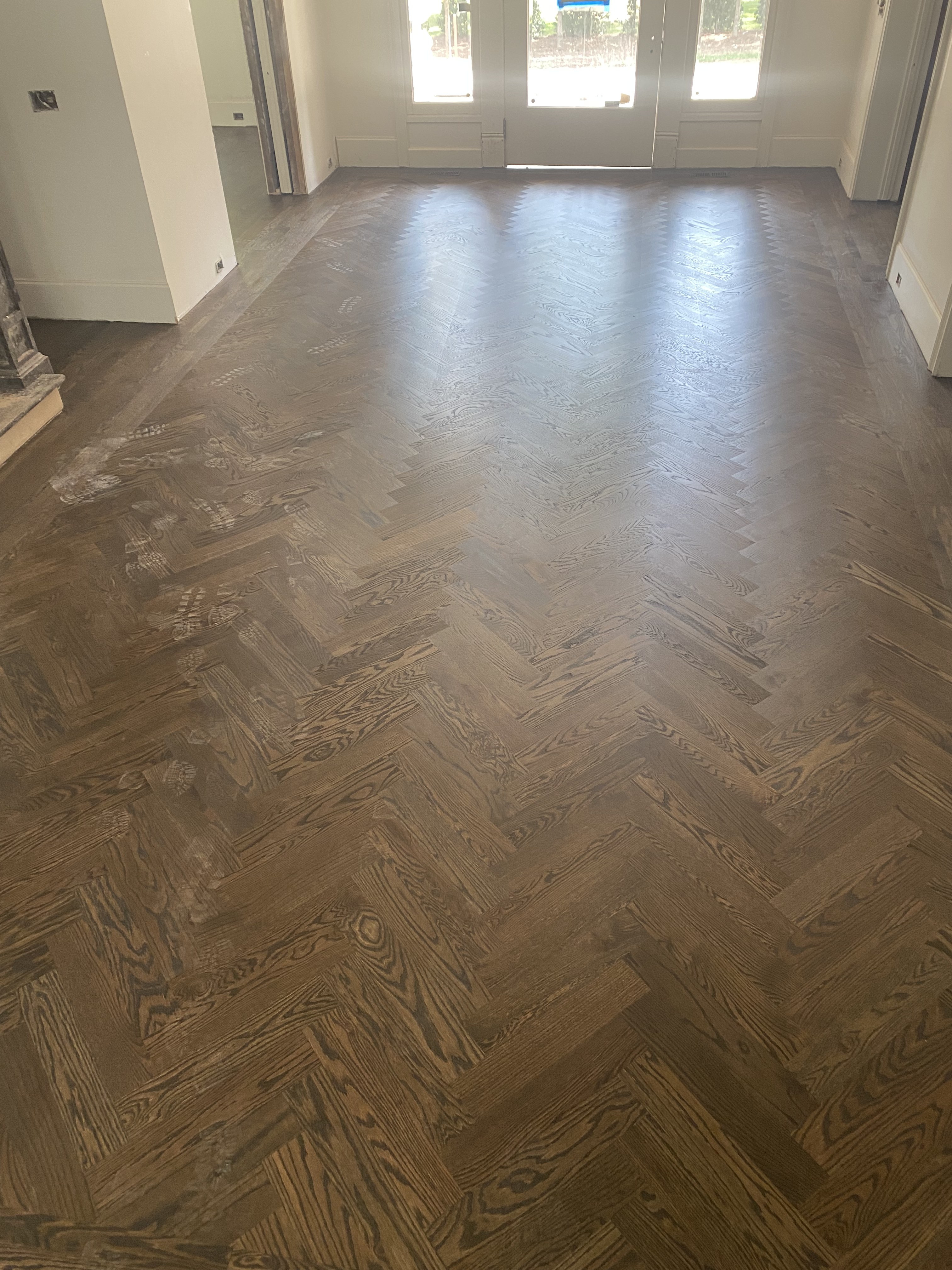 Dark herringbone hardwood flooring in a bright home entryway with French doors
