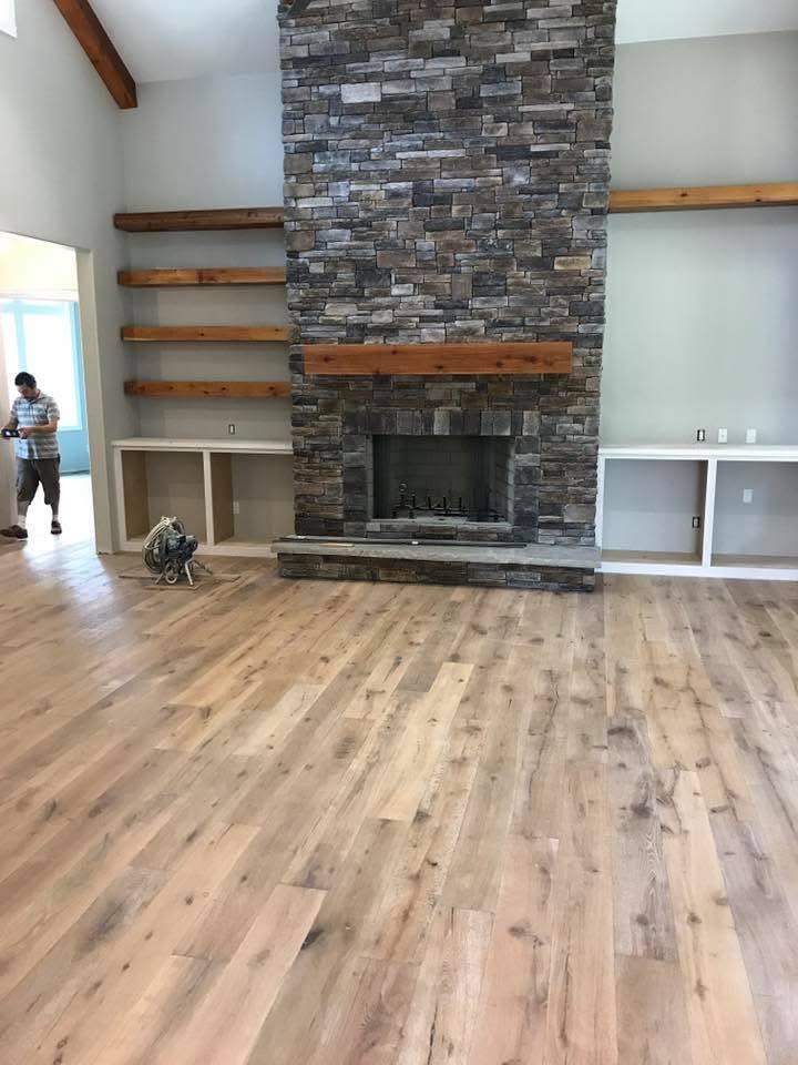 Freshly installed light hardwood flooring in a living room with stone fireplace and wood beam ceiling